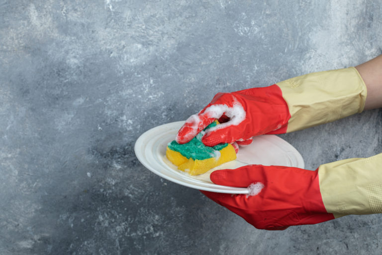 Hands in protective gloves washing plate with sponge