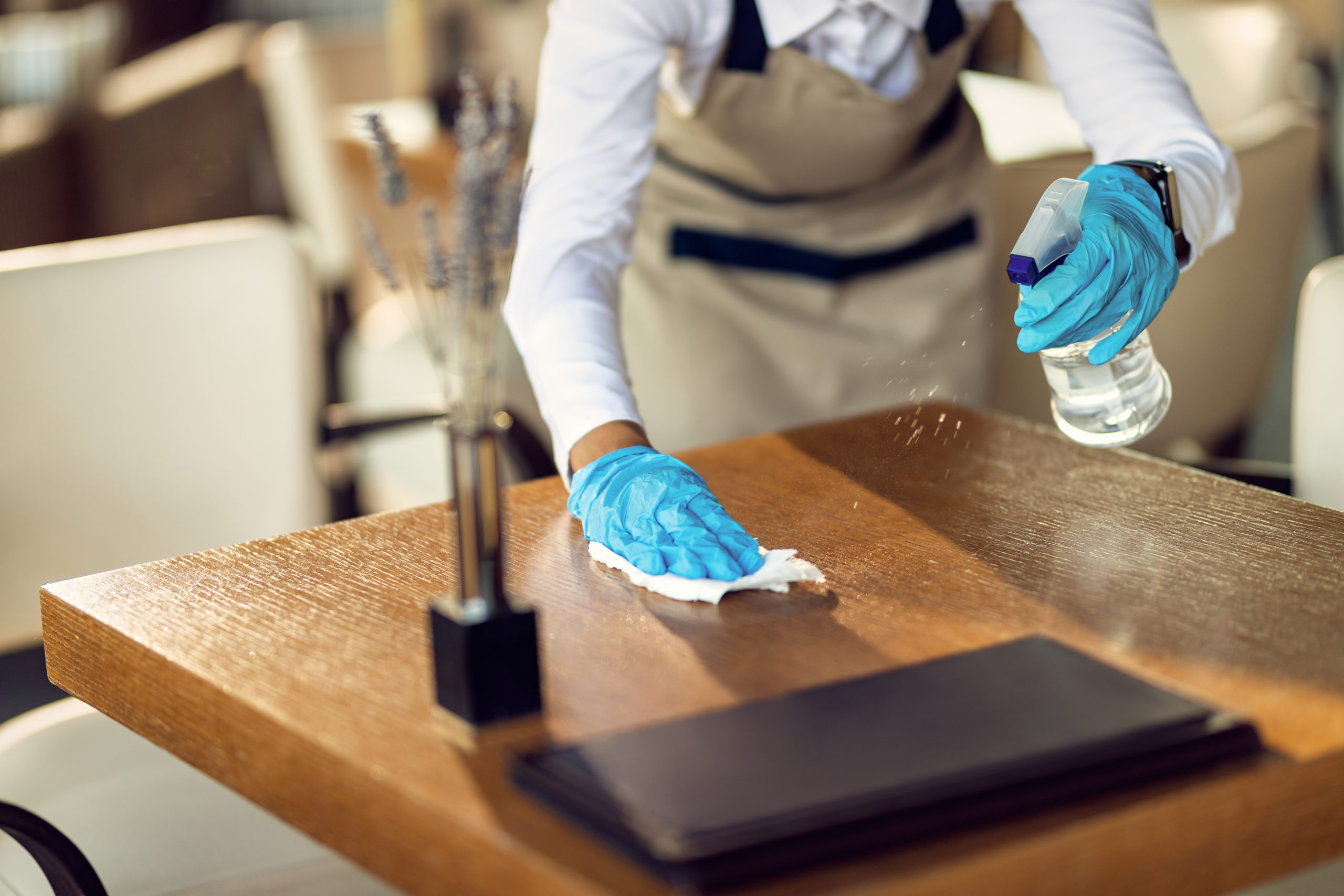 Close-up of waitress disinfecting tables in a cafe
