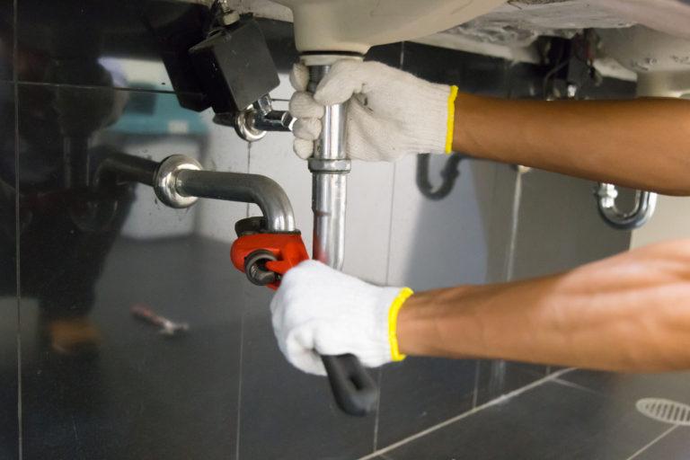 Plumber fixing white sink pipe with adjustable wrench