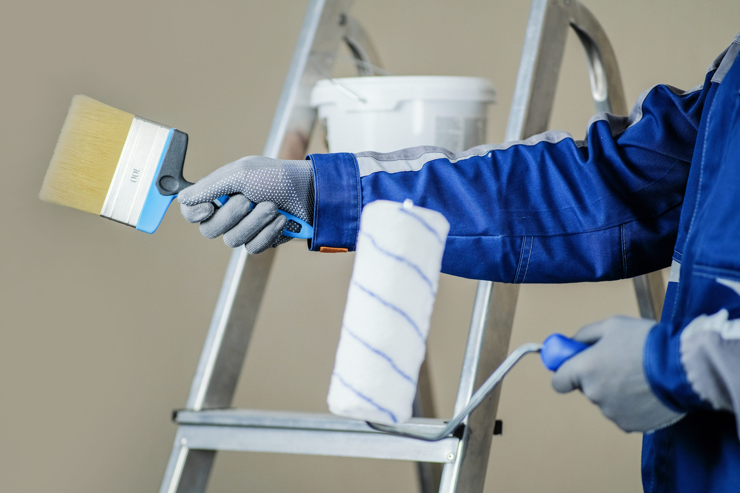 The plaster painter is ready to paint the wall. In the hands of a roller and brush. A stepladder and a bucket of paint in the background