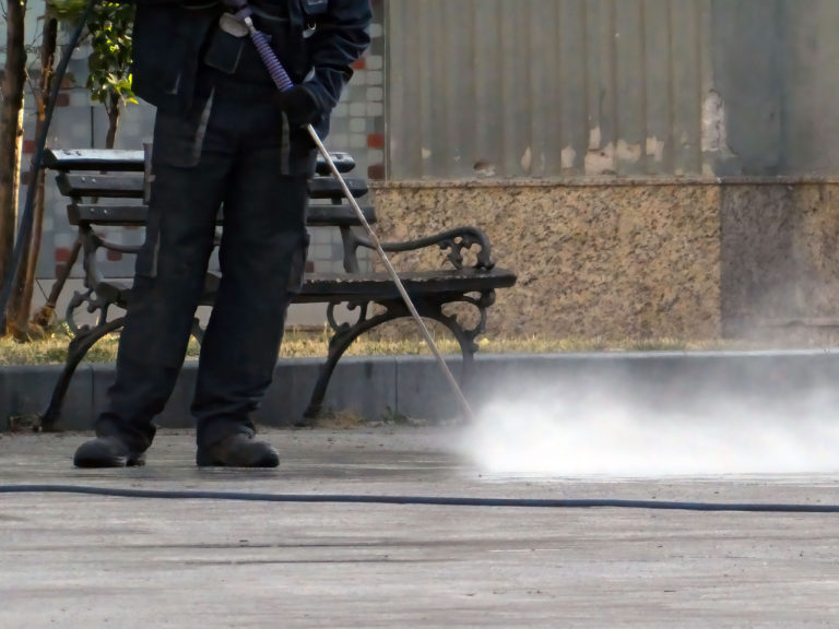 Worker cleaning the sidewalk on the street by pressing steam